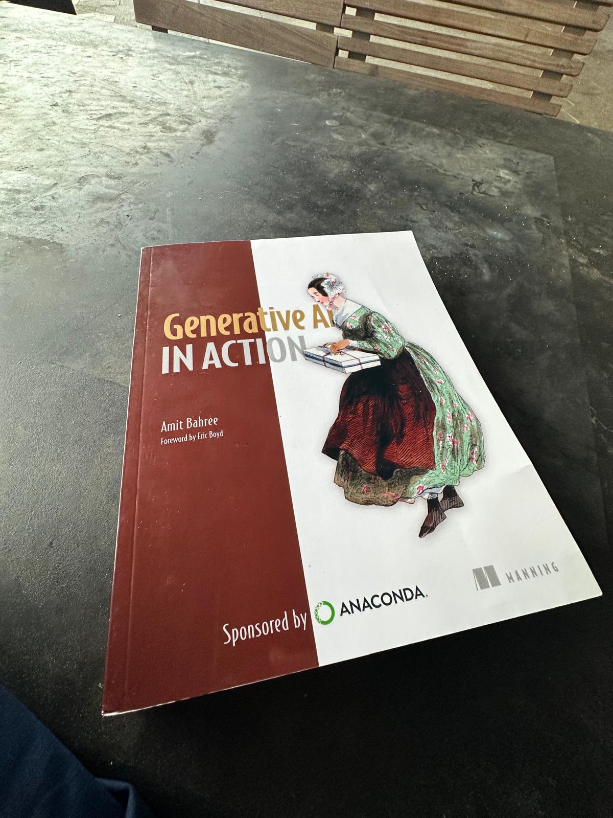 Paperback copy of Generative AI in Action by Amit Bahree on a dark table, with Sponsored by Anaconda printed on the cover
